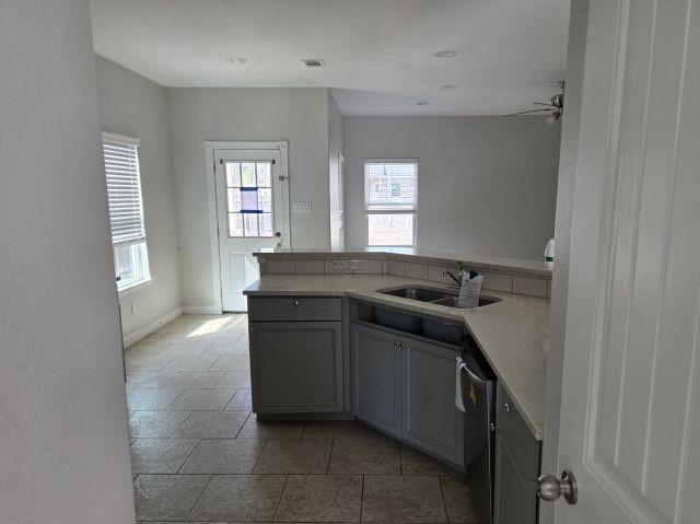 kitchen with gray cabinets, light countertops, stainless steel dishwasher, a sink, and a peninsula