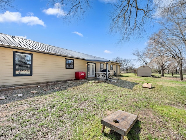 back of property with an outbuilding, metal roof, a storage shed, a yard, and french doors