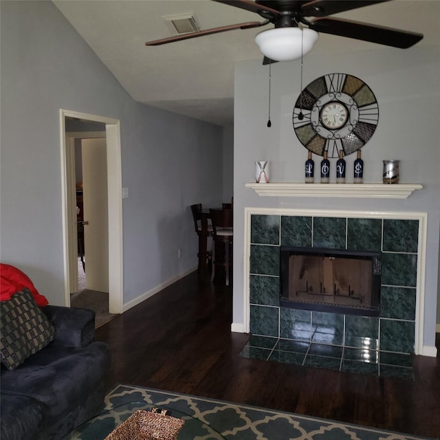 living room with dark wood-style flooring, visible vents, vaulted ceiling, a tile fireplace, and baseboards