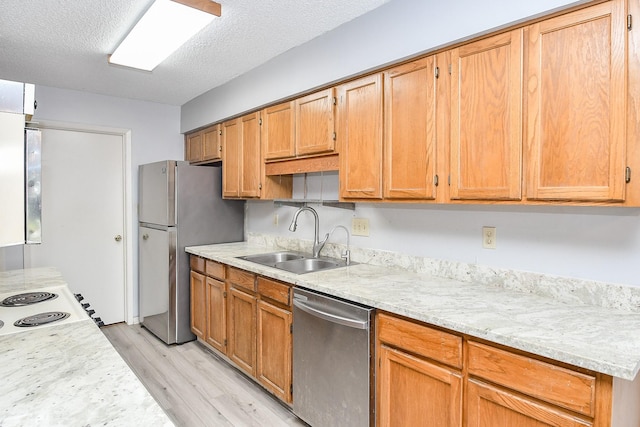 kitchen with light wood-style flooring, appliances with stainless steel finishes, light stone counters, a textured ceiling, and a sink