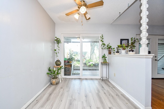 interior space featuring a textured ceiling, light wood-type flooring, a ceiling fan, and baseboards