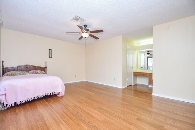 bedroom with a textured ceiling, light wood-type flooring, visible vents, and baseboards