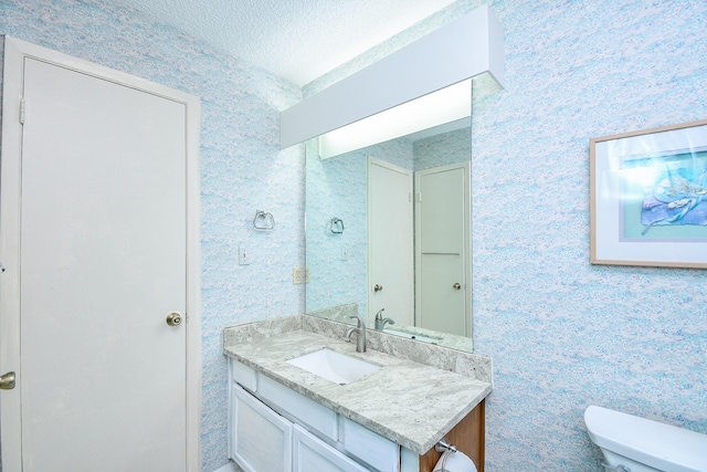 bathroom featuring toilet, wallpapered walls, a textured ceiling, and vanity