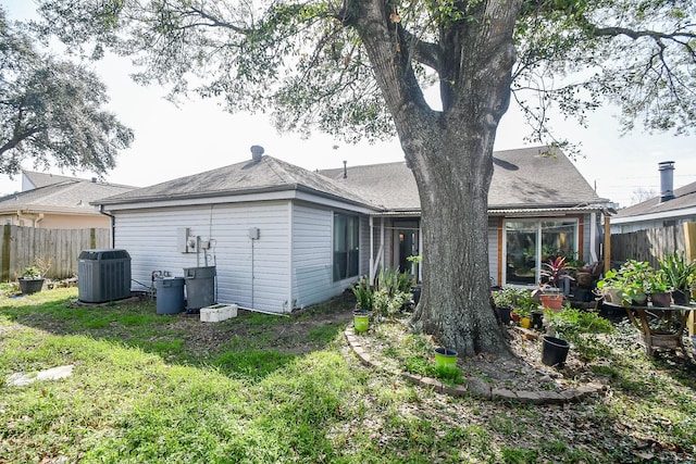 back of house featuring central AC, a yard, a shingled roof, and fence