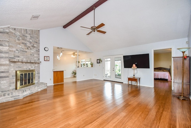 unfurnished living room with ceiling fan, beamed ceiling, a brick fireplace, and wood finished floors