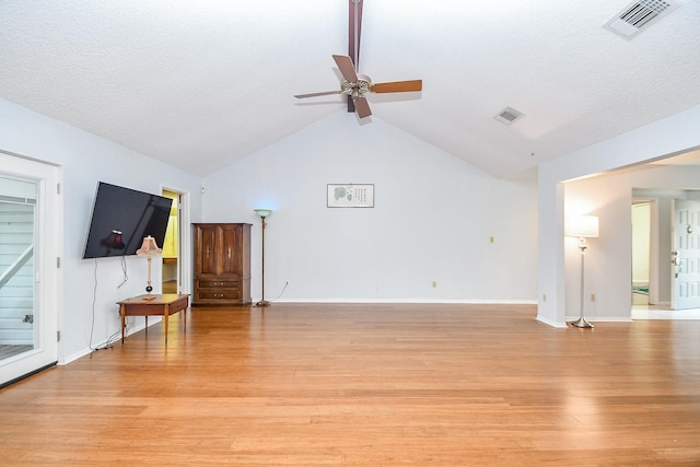 living area with lofted ceiling, a textured ceiling, visible vents, and light wood-style floors