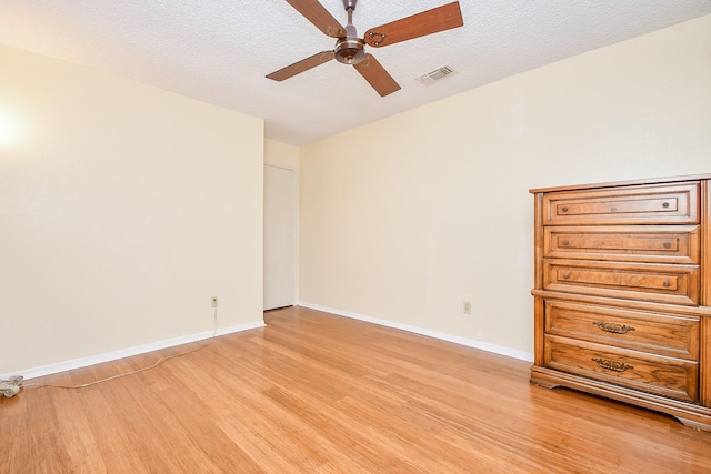 interior space featuring light wood finished floors, ceiling fan, visible vents, and a textured ceiling