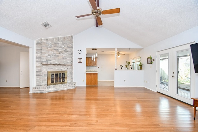 unfurnished living room with light wood-type flooring, a fireplace, visible vents, and a ceiling fan