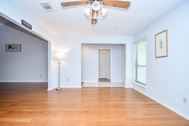 empty room featuring light wood-type flooring, baseboards, visible vents, and a textured ceiling