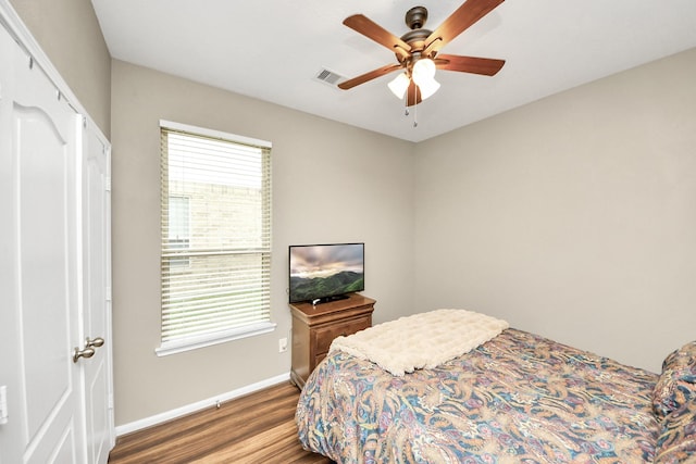 bedroom with a ceiling fan, wood finished floors, visible vents, and baseboards