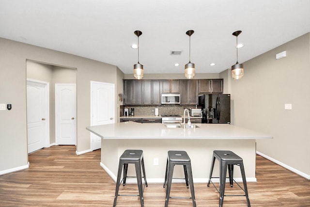 kitchen featuring light countertops, stainless steel microwave, visible vents, an island with sink, and black fridge