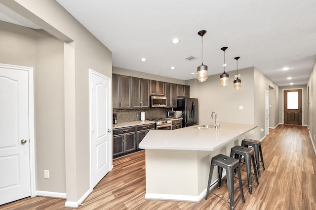 kitchen featuring a breakfast bar area, stainless steel appliances, light countertops, hanging light fixtures, and dark brown cabinetry