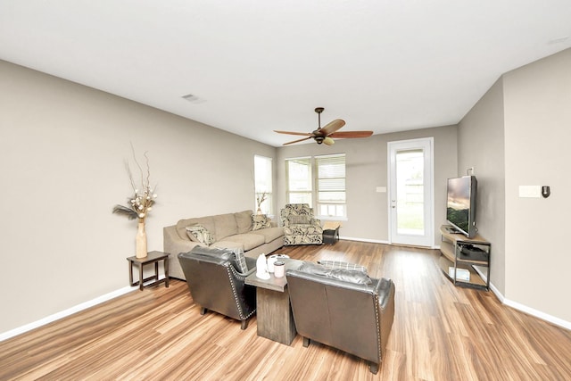 living room featuring a ceiling fan, light wood-type flooring, visible vents, and baseboards