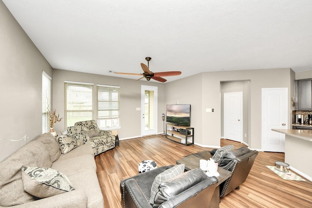 living area with baseboards, ceiling fan, and light wood finished floors