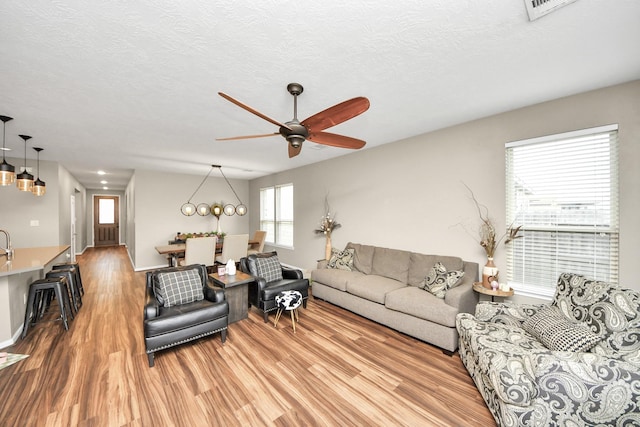 living room with light wood-style floors, ceiling fan, and a textured ceiling