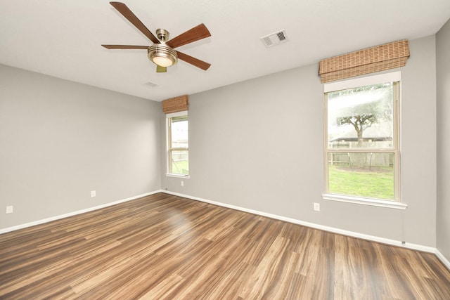 spare room with a ceiling fan, wood finished floors, visible vents, and baseboards