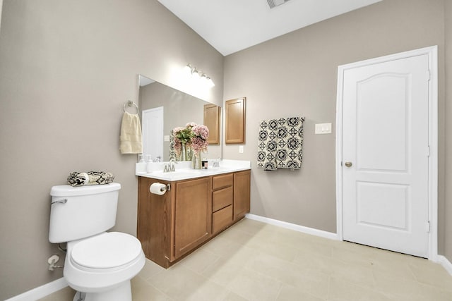 bathroom featuring toilet, double vanity, baseboards, and a sink