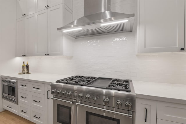 kitchen with white cabinets, light countertops, appliances with stainless steel finishes, decorative backsplash, and wall chimney exhaust hood