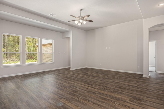 unfurnished room with arched walkways, dark wood-type flooring, a ceiling fan, visible vents, and baseboards