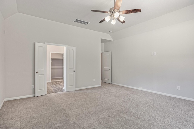 unfurnished bedroom featuring baseboards, visible vents, light colored carpet, a spacious closet, and vaulted ceiling