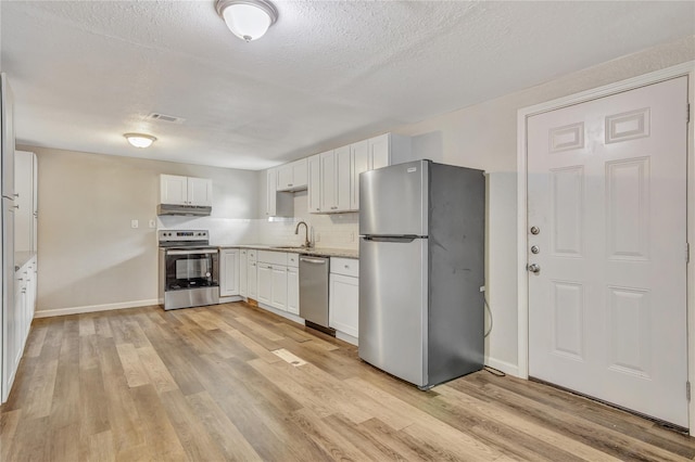 kitchen featuring under cabinet range hood, white cabinetry, light countertops, appliances with stainless steel finishes, and light wood finished floors