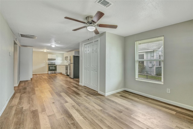 unfurnished living room featuring ceiling fan, light wood-style flooring, visible vents, and baseboards