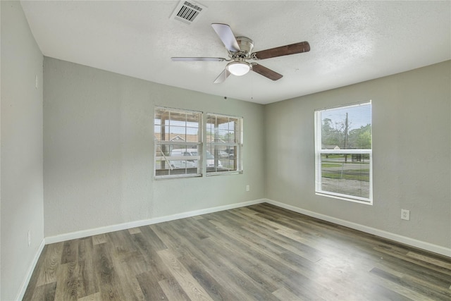 empty room with baseboards, visible vents, dark wood finished floors, ceiling fan, and a textured ceiling