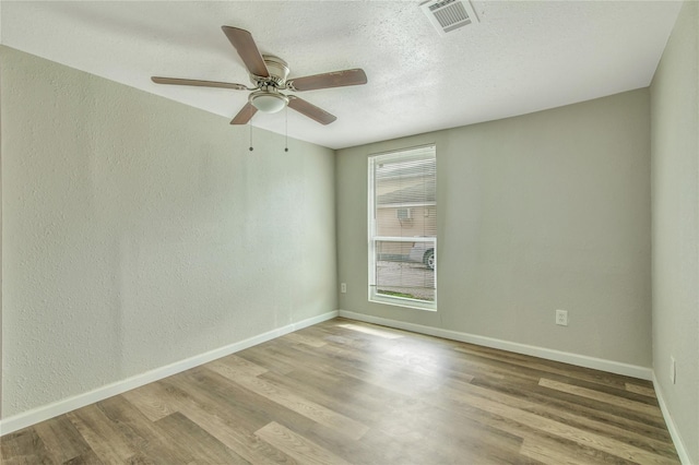 spare room featuring light wood-style floors, baseboards, visible vents, and a textured ceiling