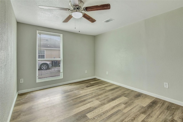empty room with visible vents, a textured wall, light wood-style flooring, and baseboards