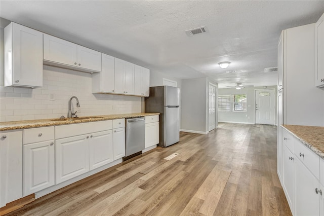 kitchen with decorative backsplash, appliances with stainless steel finishes, white cabinetry, a sink, and light wood-type flooring