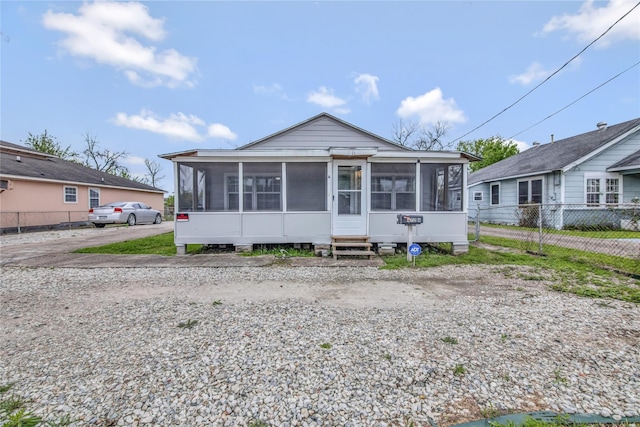 view of front of house with entry steps, a sunroom, fence, and driveway