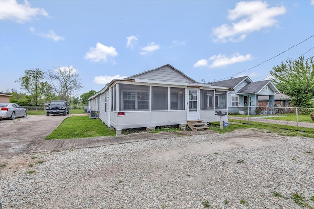 view of front facade with entry steps, a sunroom, fence, cooling unit, and driveway