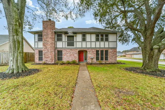 english style home featuring a front lawn, a chimney, brick siding, and stucco siding