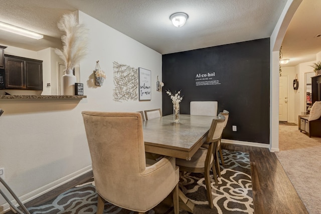 dining space with dark wood-style floors, arched walkways, a textured ceiling, and baseboards