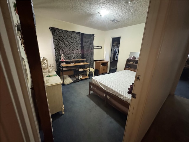 bedroom with visible vents, dark carpet, a textured ceiling, and a spacious closet