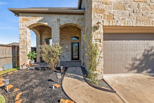 doorway to property with stone siding, an attached garage, and fence