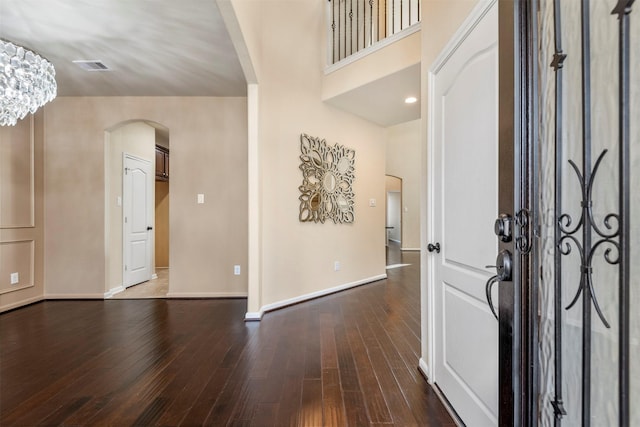 entrance foyer featuring arched walkways, dark wood-type flooring, visible vents, and baseboards