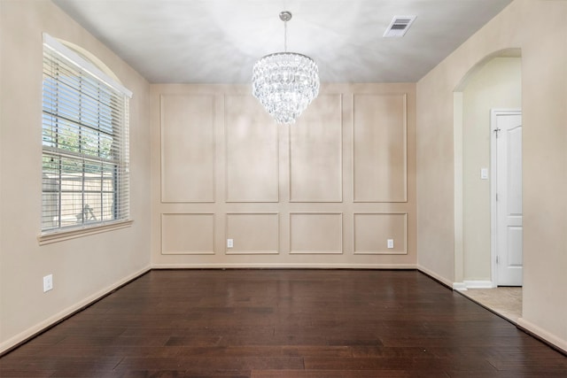 spare room with dark wood-style floors, arched walkways, visible vents, an inviting chandelier, and baseboards