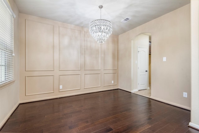 spare room featuring arched walkways, a chandelier, dark wood-type flooring, visible vents, and baseboards