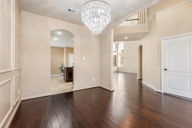 empty room with visible vents, arched walkways, baseboards, wood finished floors, and an inviting chandelier