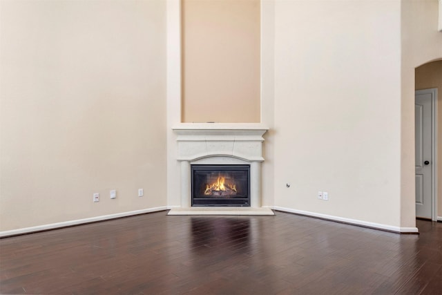 unfurnished living room with baseboards, dark wood finished floors, arched walkways, and a glass covered fireplace