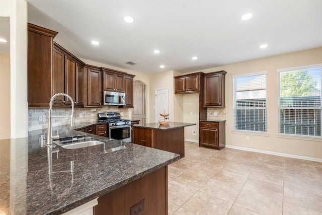 kitchen with stainless steel appliances, a peninsula, a sink, dark stone counters, and tasteful backsplash