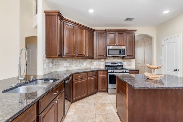 kitchen featuring appliances with stainless steel finishes, dark stone countertops, and a sink