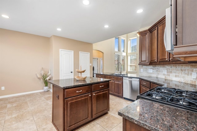 kitchen with tasteful backsplash, arched walkways, dishwasher, a kitchen island, and a sink