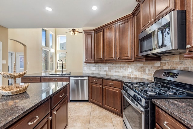 kitchen with light tile patterned floors, tasteful backsplash, dark stone counters, appliances with stainless steel finishes, and a sink