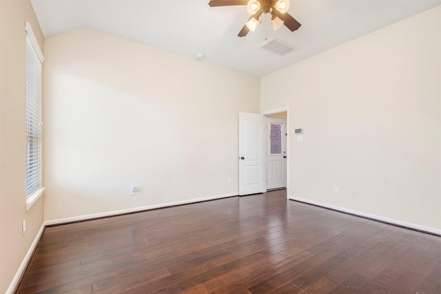 empty room featuring dark wood-style floors, visible vents, baseboards, and vaulted ceiling