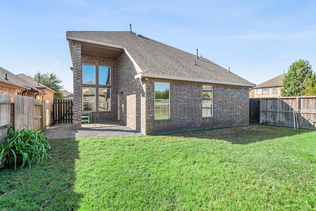 rear view of property featuring brick siding, a lawn, a fenced backyard, and roof with shingles