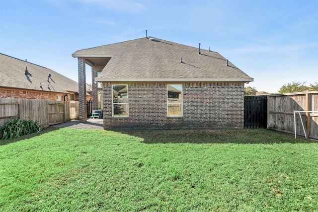 back of house featuring brick siding, a fenced backyard, a shingled roof, and a yard