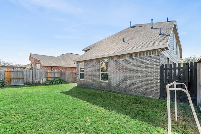 back of property featuring brick siding, a yard, a fenced backyard, and roof with shingles