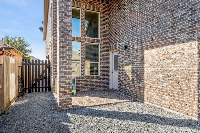 view of exterior entry with a gate, fence, a patio, and brick siding